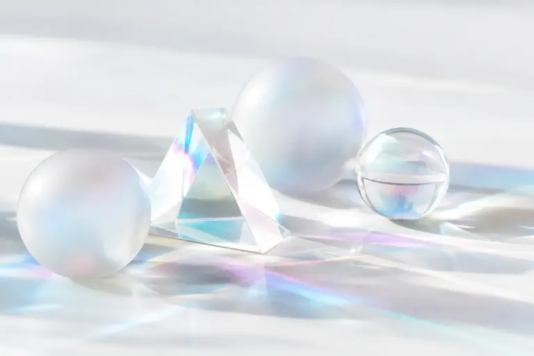 Prisme de verre et sphères dépolies projetant des reflets irisés sur fond blanc
